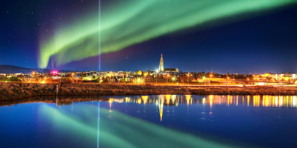 Green northern lights over Reykjavík reflected in the water, Iceland
